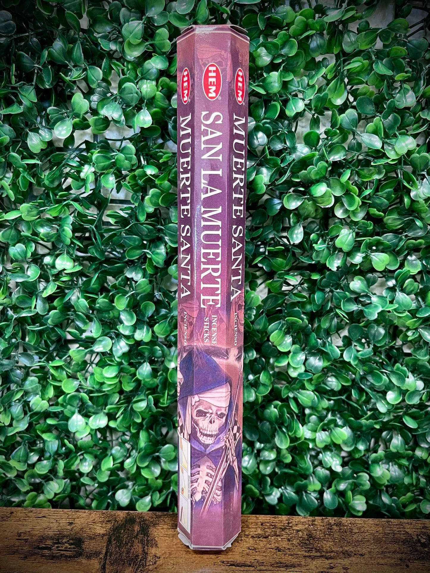 Hexagonal incense stick container with 'Muerte Santa' design on a green leafy background