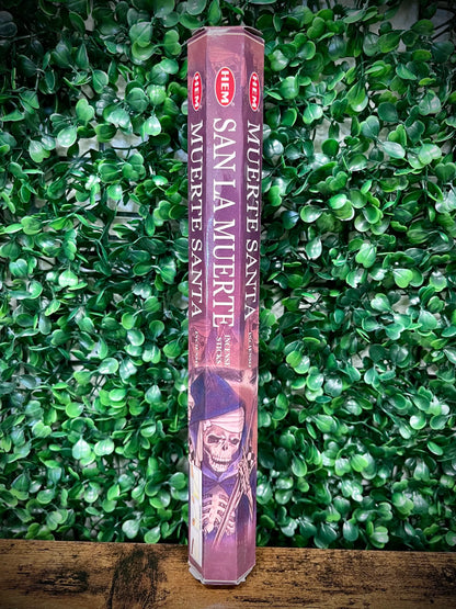 Hexagonal incense stick container with 'Muerte Santa' design on a green leafy background