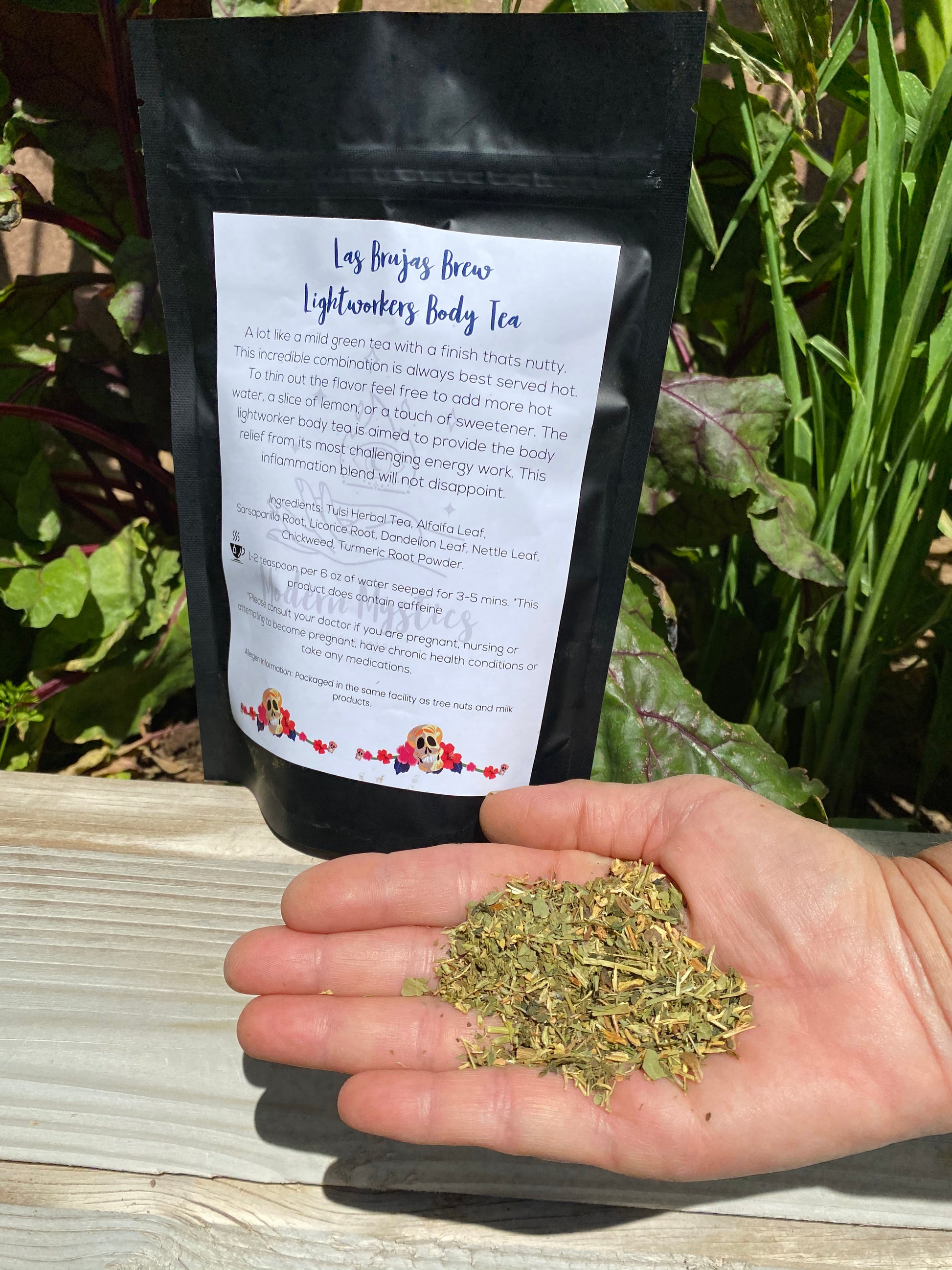 Tea package with a label held by a hand with tea leaves on a wooden surface with plants in the background