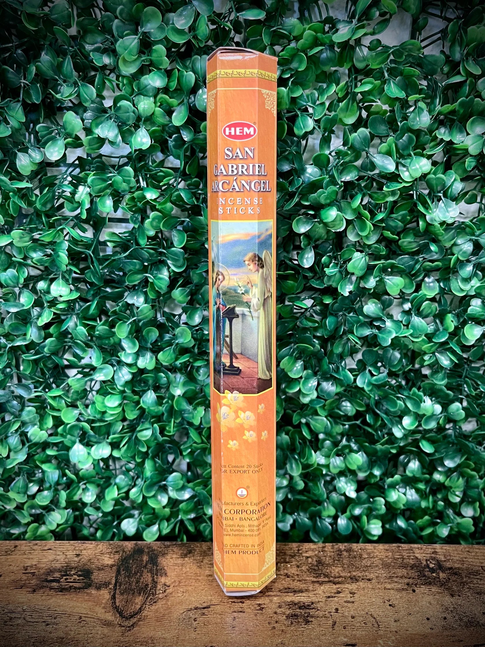 Hem San Abril Incense stick packaging on a wooden surface with green foliage in the background