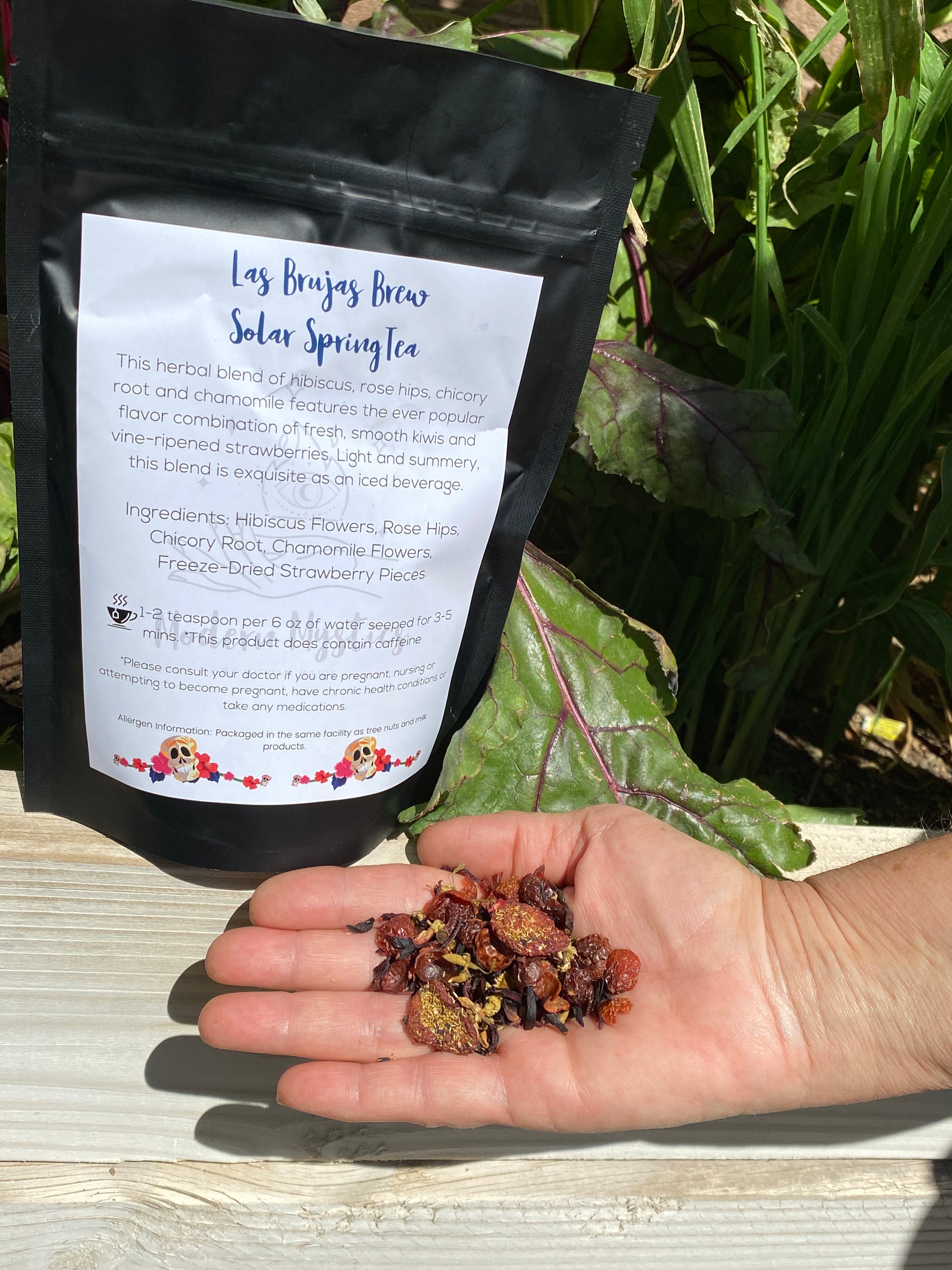 Hand holding dried herbs in front of a black tea bag with text on a natural background